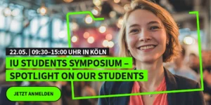 A smiling student in front of the announcement banner for the IU Students Symposium 2026 in Cologne.