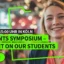 Eine lächelnde Studentin vor dem Ankündigungsbanner zum IU Students Symposium 2026 in Köln.