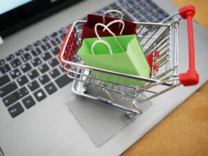 A small shopping cart with a red and green paper bag on a laptop keyboard, symbolizing sustainable online retail and re-commerce in Cologne.